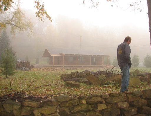 A man is standing on a stone wall in front of a house in the fog.