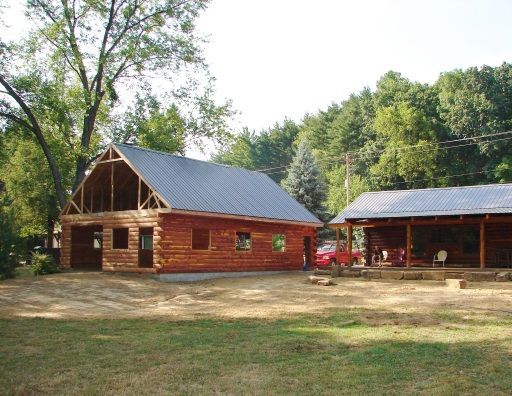 A red car is parked in front of a log cabin
