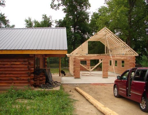 A red van is parked in front of a log cabin under construction