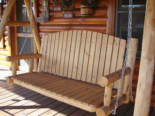 A wooden swing is sitting on a porch in front of a log cabin.