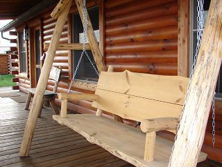 A wooden swing is sitting on a wooden deck in front of a log cabin.