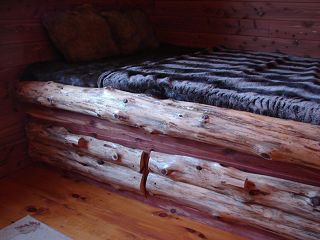 A log bed with a blanket on top of it in a wooden room.