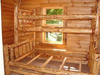 A wooden bunk bed in a log cabin with two windows.