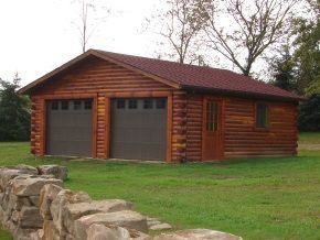 A log cabin with two garage doors is sitting in the middle of a lush green field.