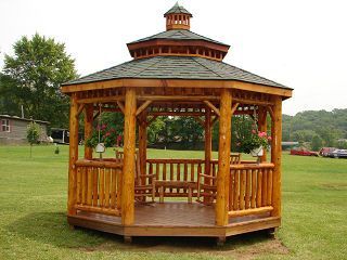 A wooden gazebo is sitting in the middle of a grassy field.