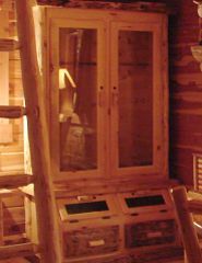 A wooden cabinet with glass doors and drawers in a log cabin.
