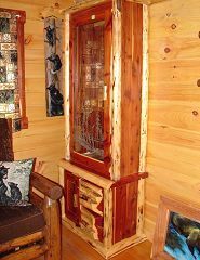 A wooden cabinet with a glass door is in a living room next to a chair.