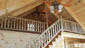A wooden staircase leading up to a loft with a ceiling fan hanging from the ceiling.