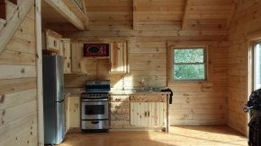 A kitchen in a log cabin with a stove , refrigerator , sink and window.