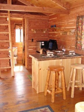 A wooden cabin with a kitchen and two stools
