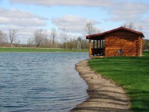 A small wooden house is sitting on the shore of a lake.