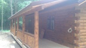 A log cabin with a screened in porch in the woods.