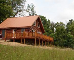 A log cabin with a large deck in the middle of a field