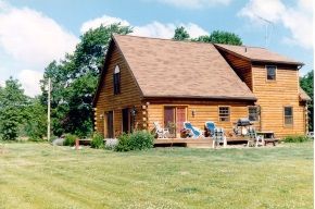 A large log cabin sits in the middle of a lush green field