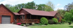 A large log cabin with a red roof and a porch surrounded by trees.