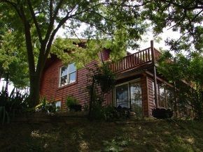 A red house with a balcony is surrounded by trees.