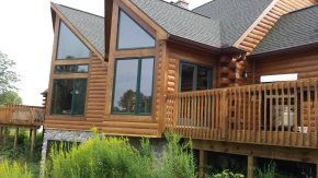 A large log cabin with a large deck and lots of windows.