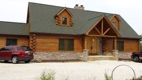 A red car is parked in front of a log cabin.