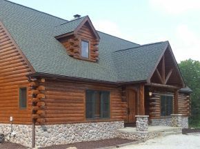 A large log cabin with a green roof and stone siding.