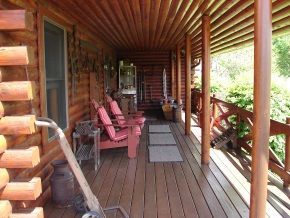 A wooden porch with red chairs and a wheelbarrow