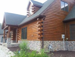 A large log cabin with a stone wall and a black roof