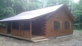 A log cabin with a porch in the middle of a forest.