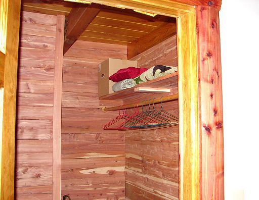 A wooden closet with clothes and a box on the shelf
