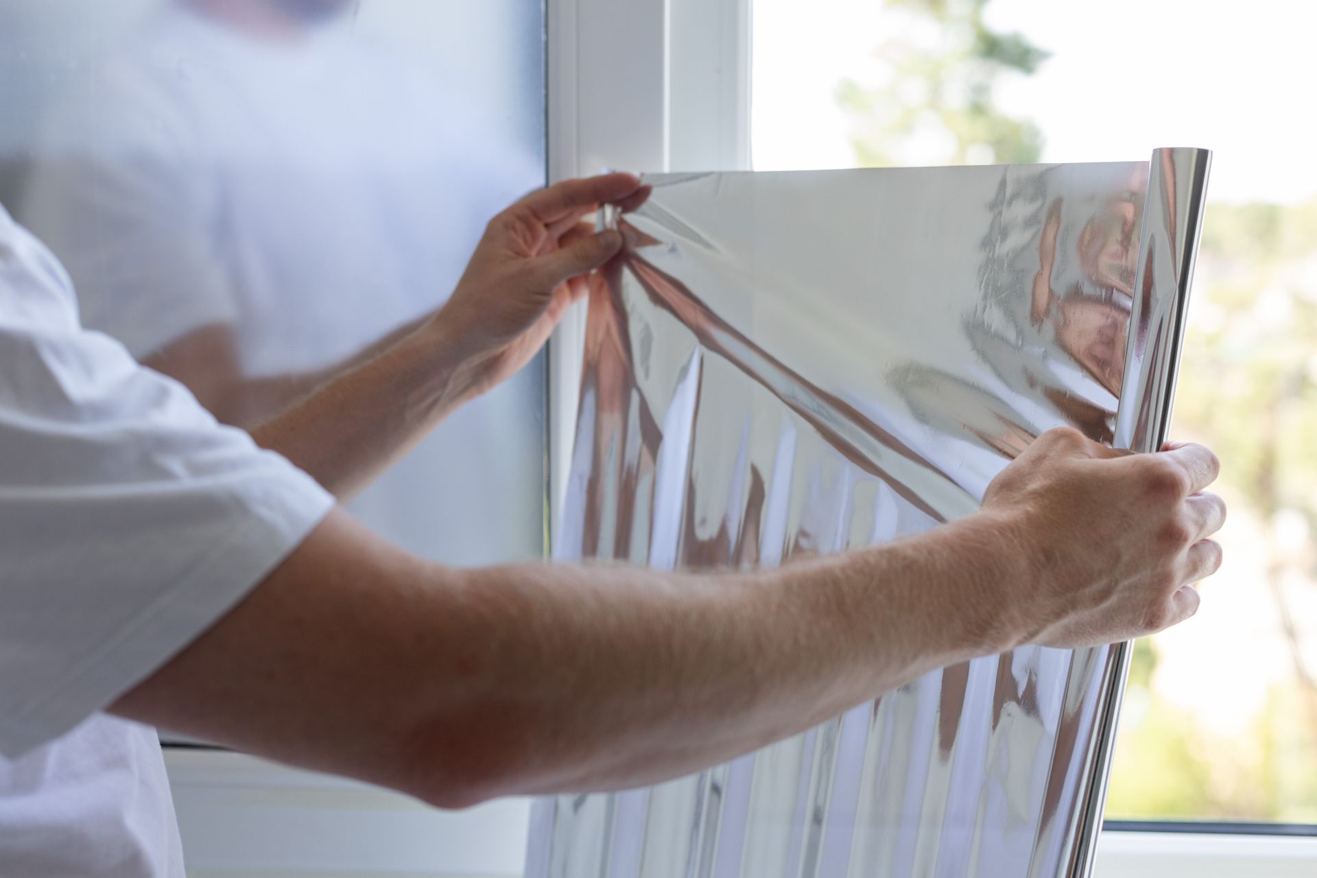 Person holding a large reflective sheet near a window, adjusting its edge.