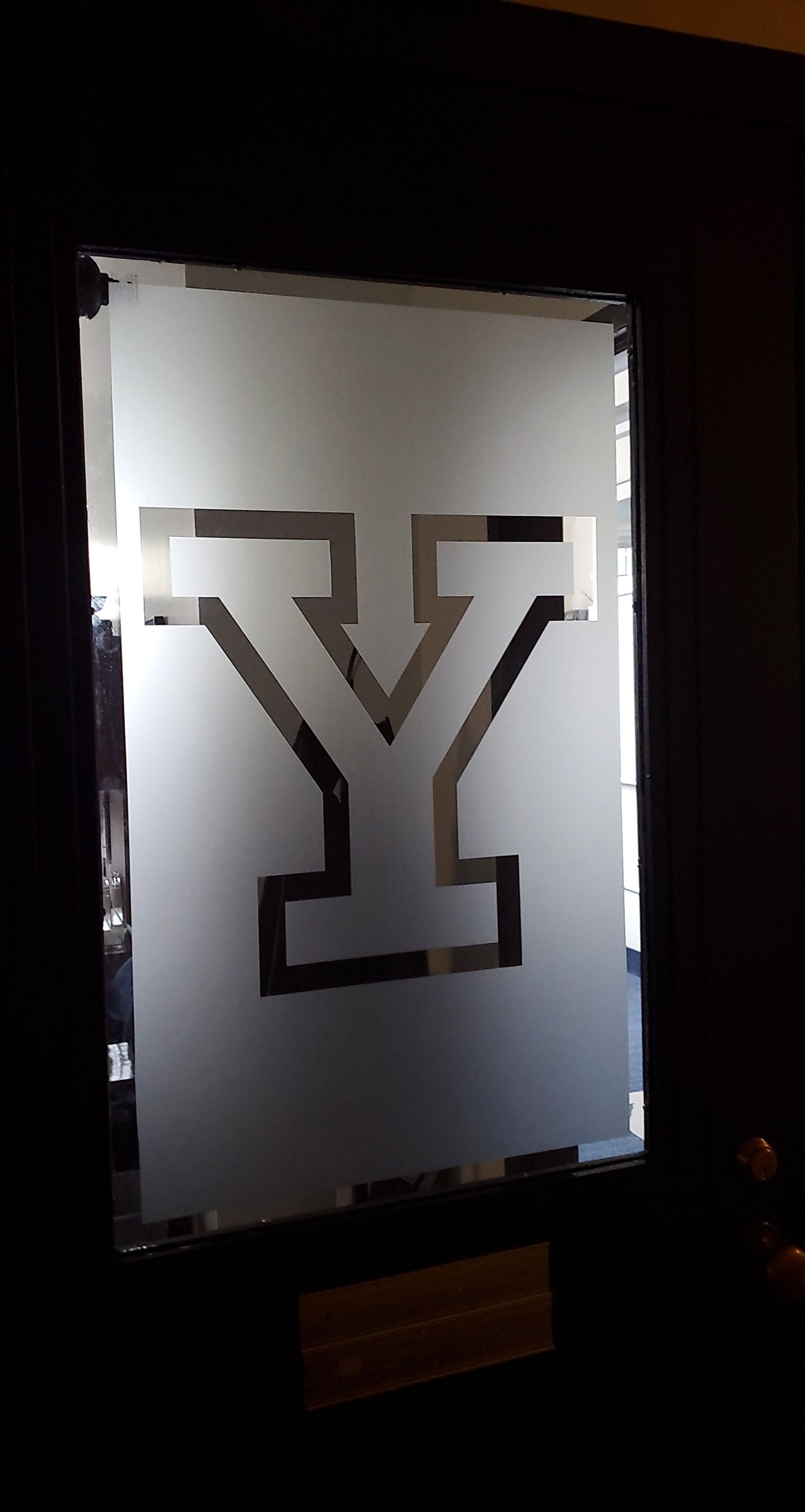 Frosted glass panel with a large dark letter Y and a glowing edge in a dim room
