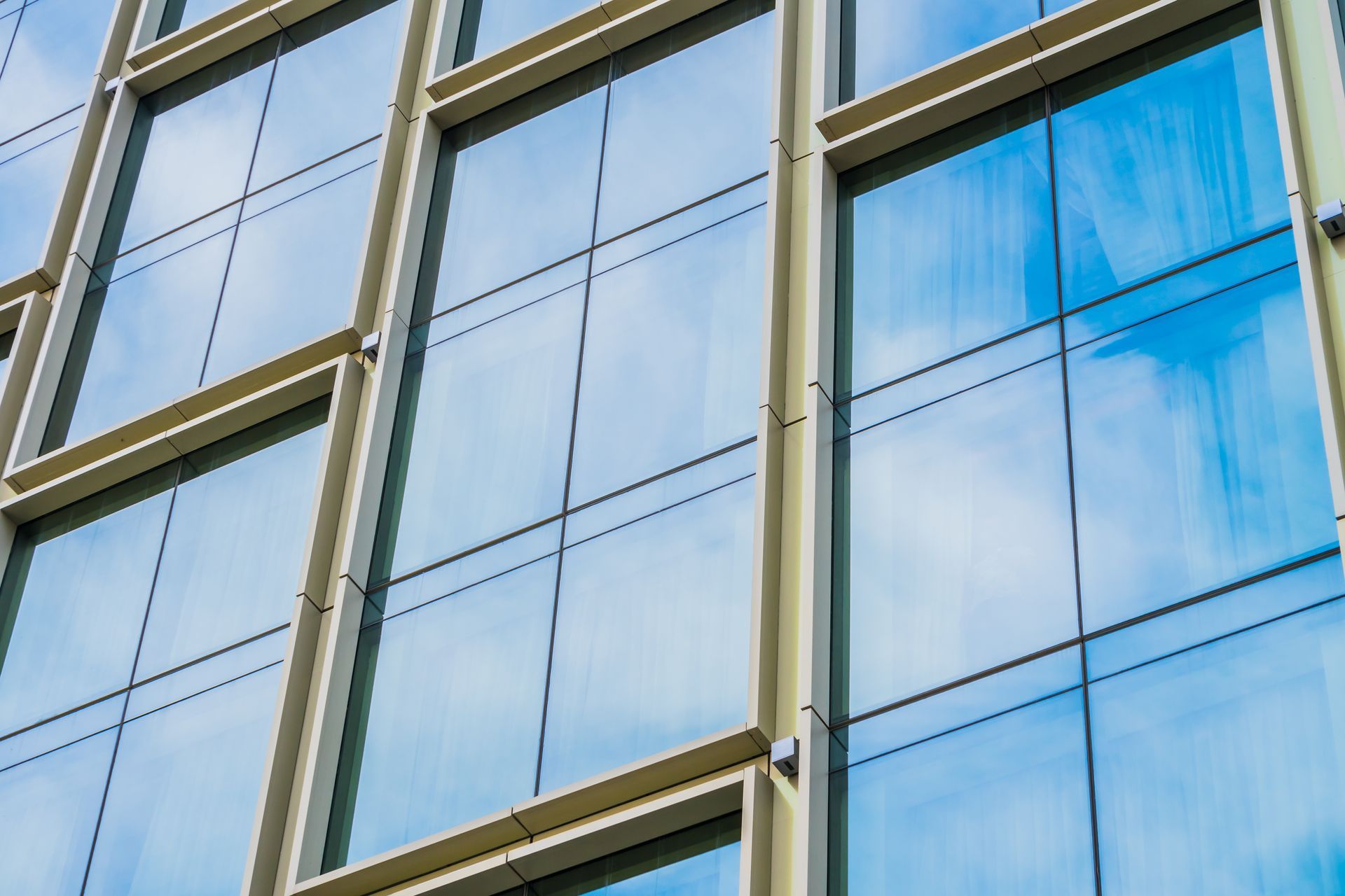 Reflective glass windows on a modern building facade against a blue sky with clouds