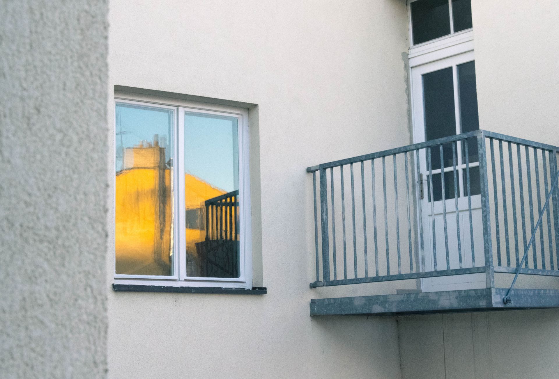 Apartment exterior with a small balcony and window reflecting a yellow building