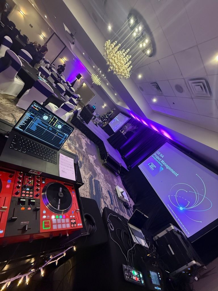 DJ booth with laptop, turntables, and purple-lit event hall with projector screen