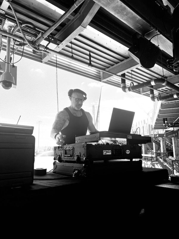 DJ at a booth with a laptop and mixing gear under an industrial ceiling