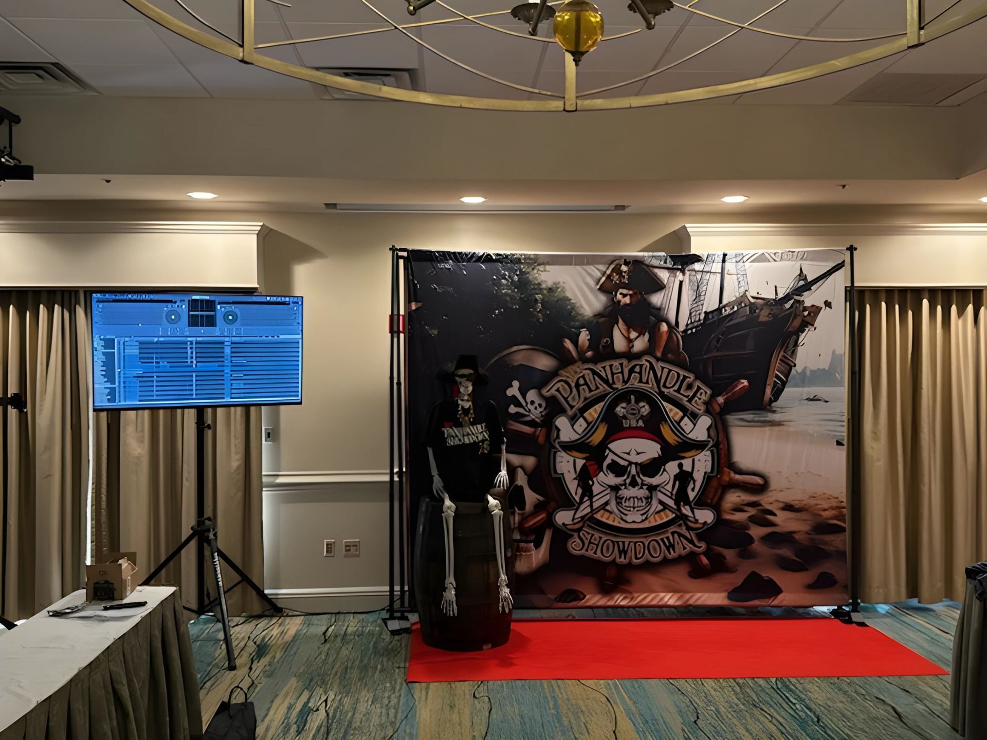 Conference display with a red-carpet stage, large graphic backdrop, and a monitor on a tripod in a hotel ballroom
