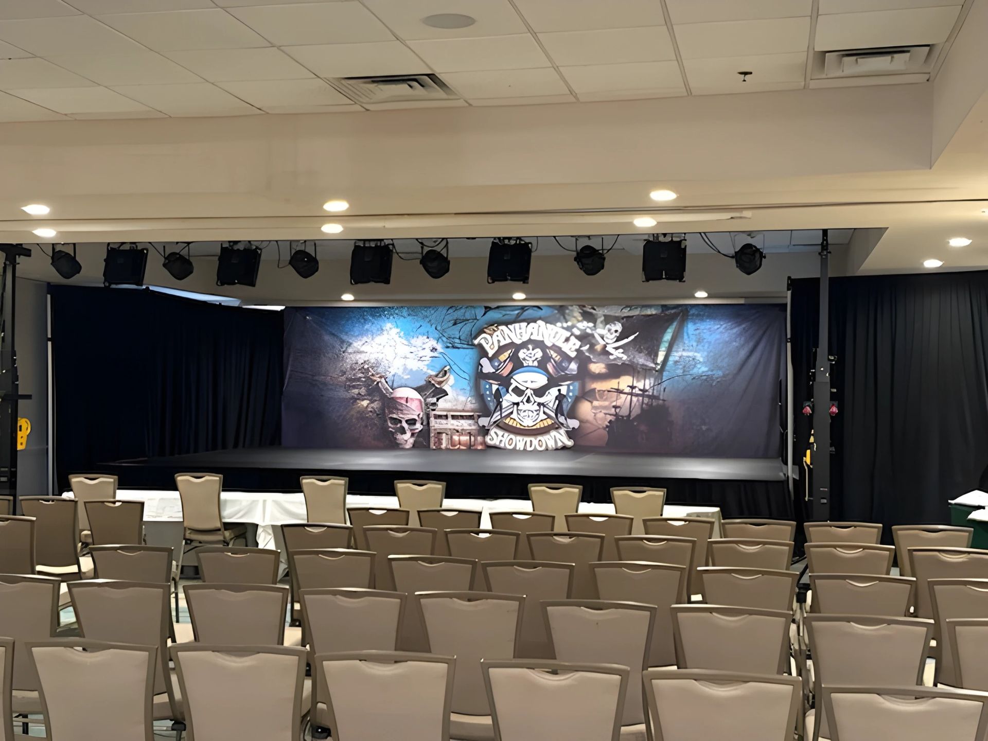 Empty event stage with chairs facing a large banner and stage lights in a banquet hall