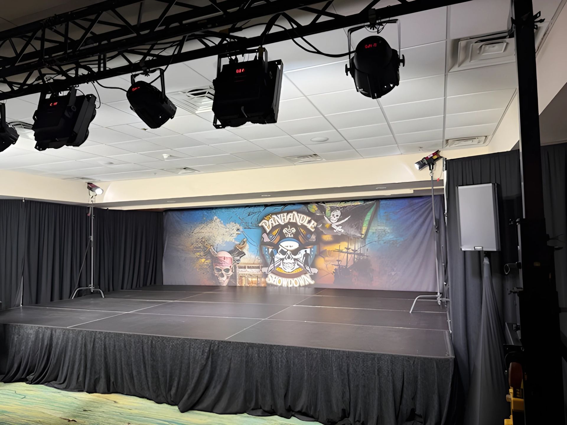 Empty stage with black curtains, overhead lights, and a colorful mural backdrop in a small theater