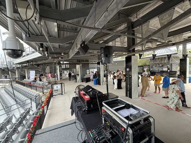 Indoor stadium concourse with equipment cases, people walking, and seating under exposed steel beams.