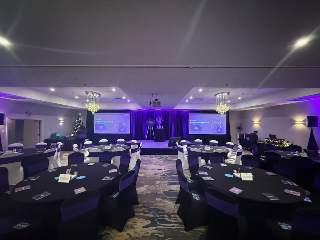Empty banquet hall set for an event, with round tables, purple lighting, and a stage with screens at the front