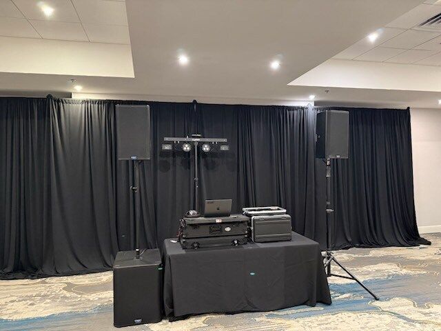 Audio equipment setup on a black-draped table in a conference room with speaker stands and curtains