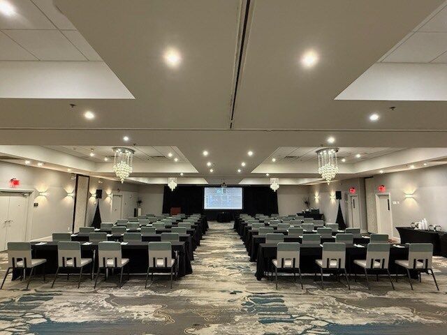 Empty conference room with rows of chairs facing a presentation screen and stage.