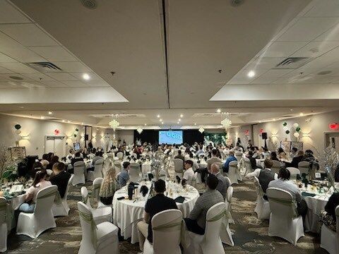 Banquet hall with round tables full of seated guests at a formal event, with a screen at the front