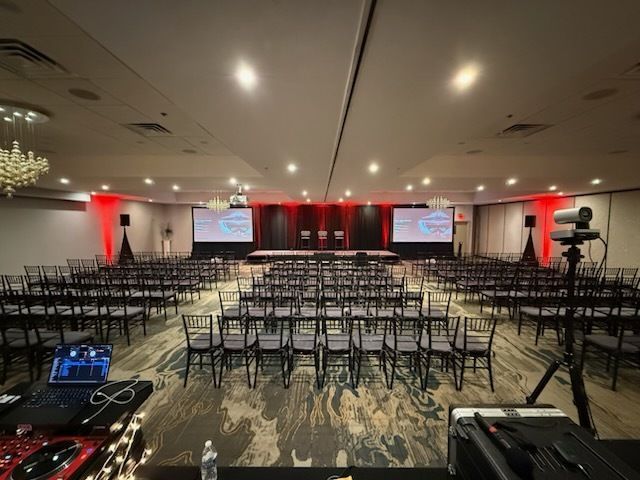 Conference ballroom with rows of empty chairs facing a lit stage and projection screens