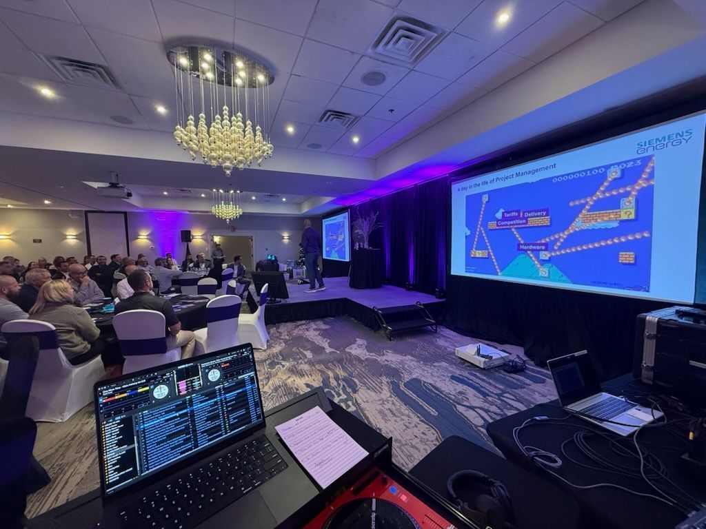 Conference audience facing stage with large map display, purple lighting, and laptop in foreground