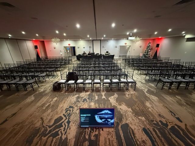 Empty conference hall with rows of chairs facing a stage and a presentation screen in front.