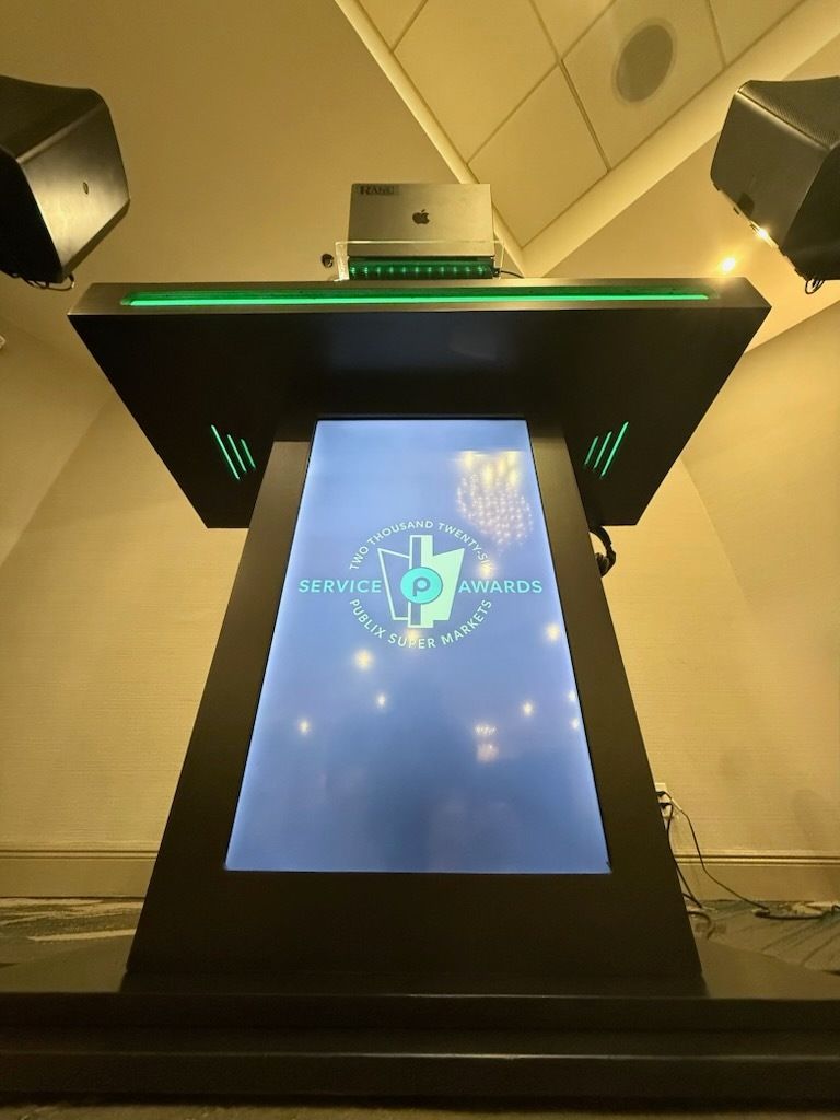 Interactive kiosk with glowing green accents and a blue touchscreen in a hallway