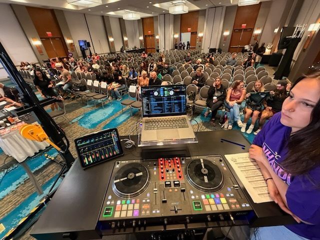 DJ booth overlooking a seated conference audience in a hotel ballroom