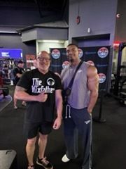 Two men posing together in a gym, one in a black T-shirt and one in a gray tank top.