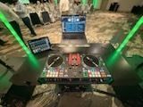 DJ setup with laptop and dual turntables in a stadium, viewed from behind the booth