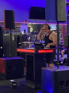 DJ at a club booth under blue and purple lights, wearing headphones and touching his face.