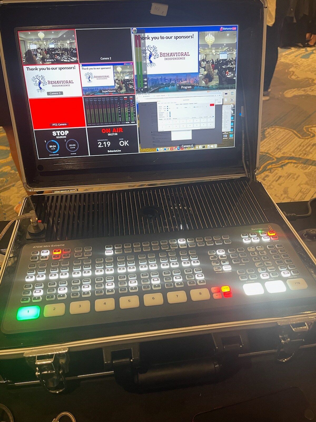 Multiview video production console with many lit buttons and several monitor screens in a dim room